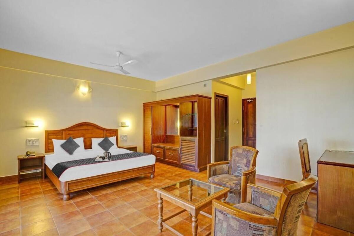 A hotel room with a wooden bed, a glass coffee table, a chair, a wardrobe, and a desk.