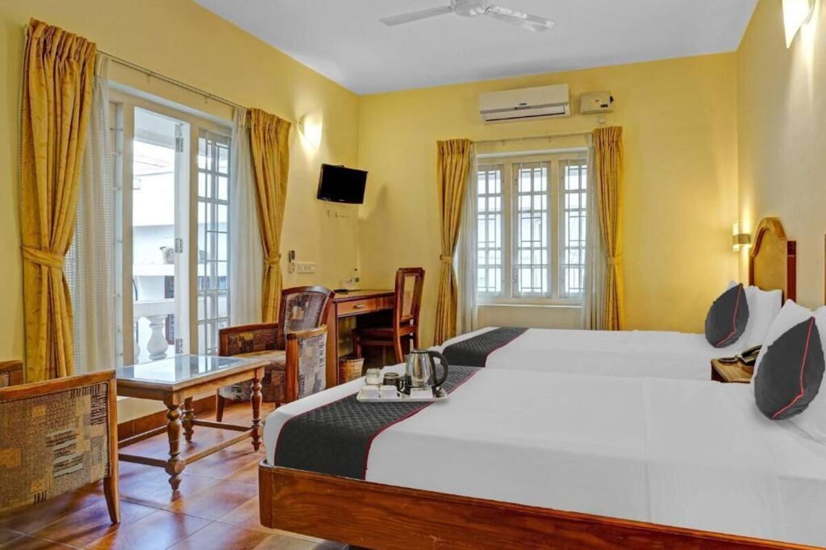 A hotel room with two beds, a desk, a chair, and an air conditioning unit.