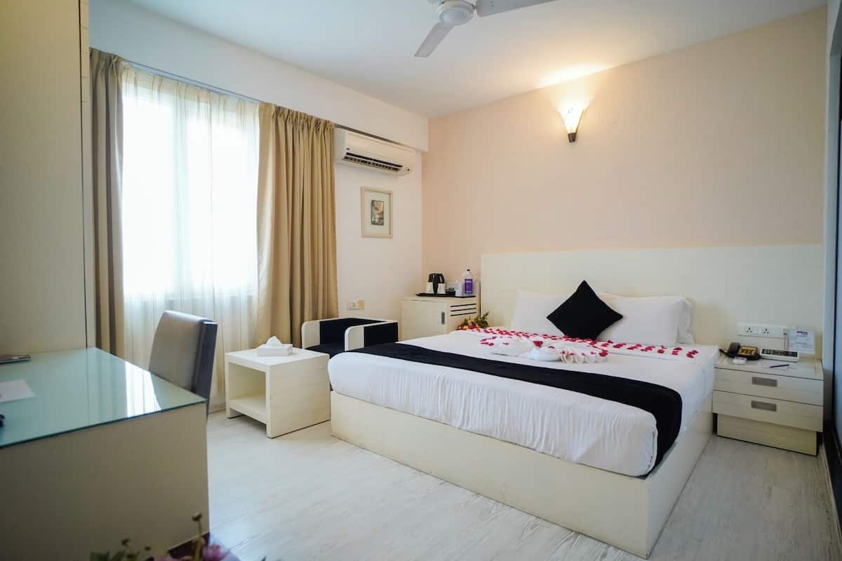 A hotel room with a bed, bedside table, nightstand, desk, chair, and an air conditioning unit.