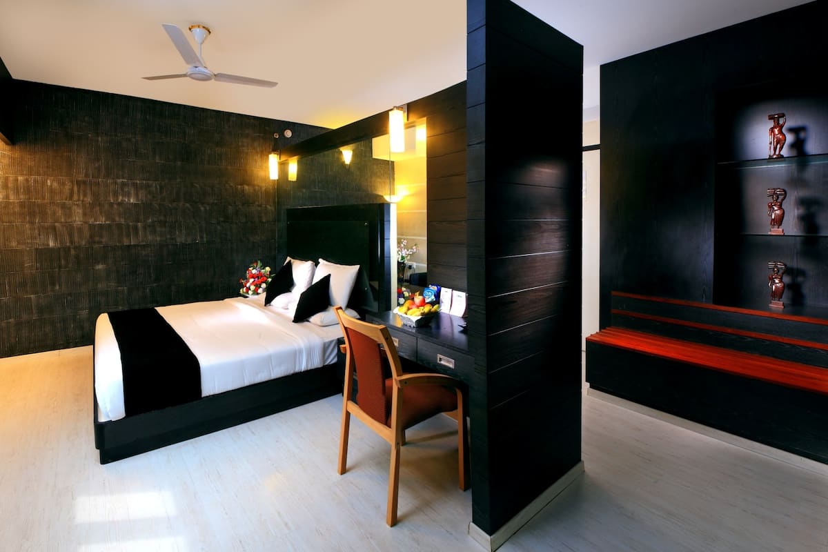 A modern bedroom with a bed, desk, chair, and a dark accent wall with shelves.