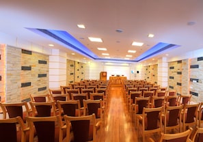 Un salón de conferencias con filas de sillas, una larga mesa y un atril al frente.