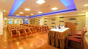 A conference room with rows of chairs, a round table with a white tablecloth, and a stone wall with a wooden panel design. - Olive Eva (Kanayannur)