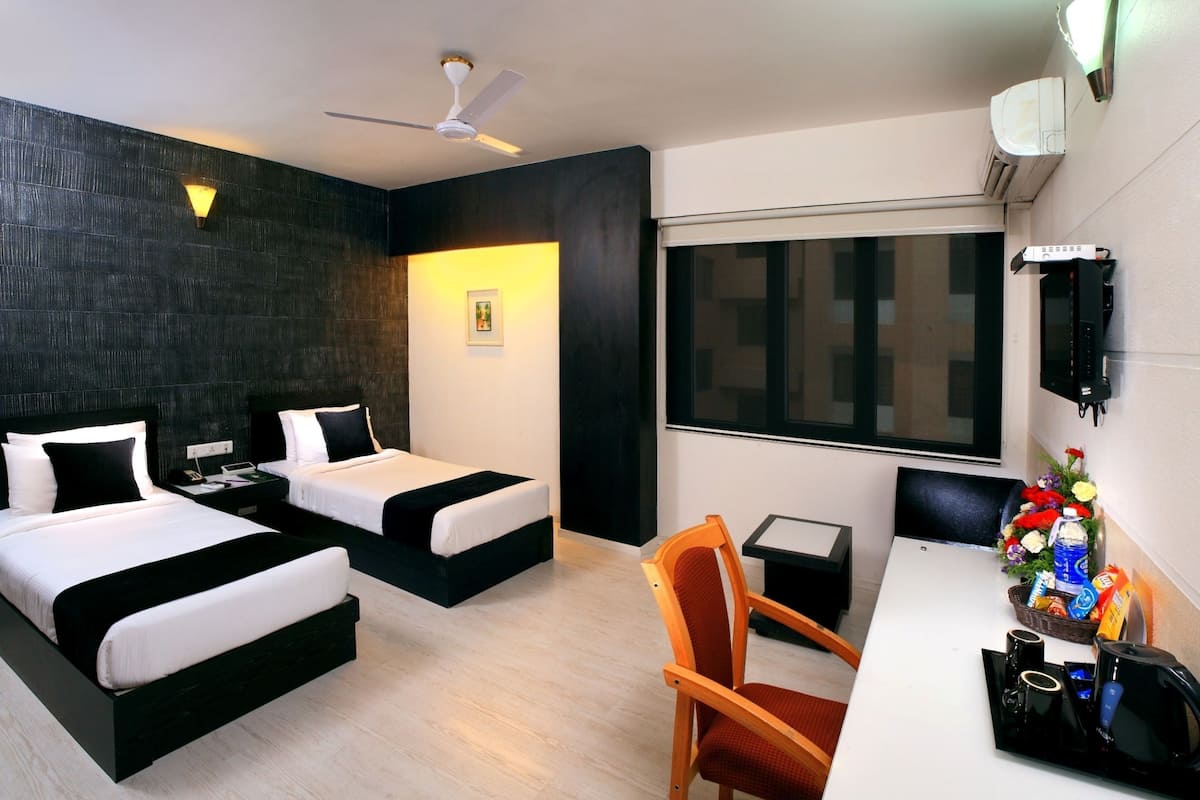 A hotel room with two beds, a desk, a chair, a ceiling fan, a window, and a wall-mounted air conditioner.