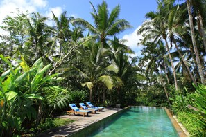 A poolside area with lounge chairs and palm trees. - Swarapadi Villa (Ubud)