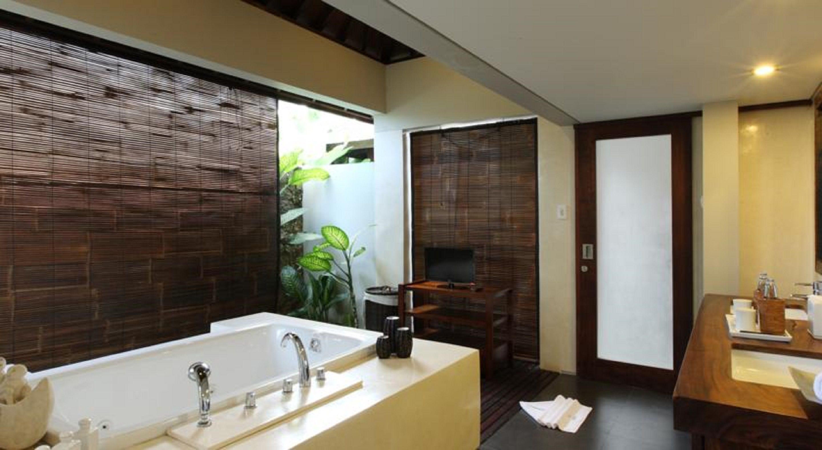 A modern bathroom with a large bathtub, a vanity with a sink, and a television in the corner.