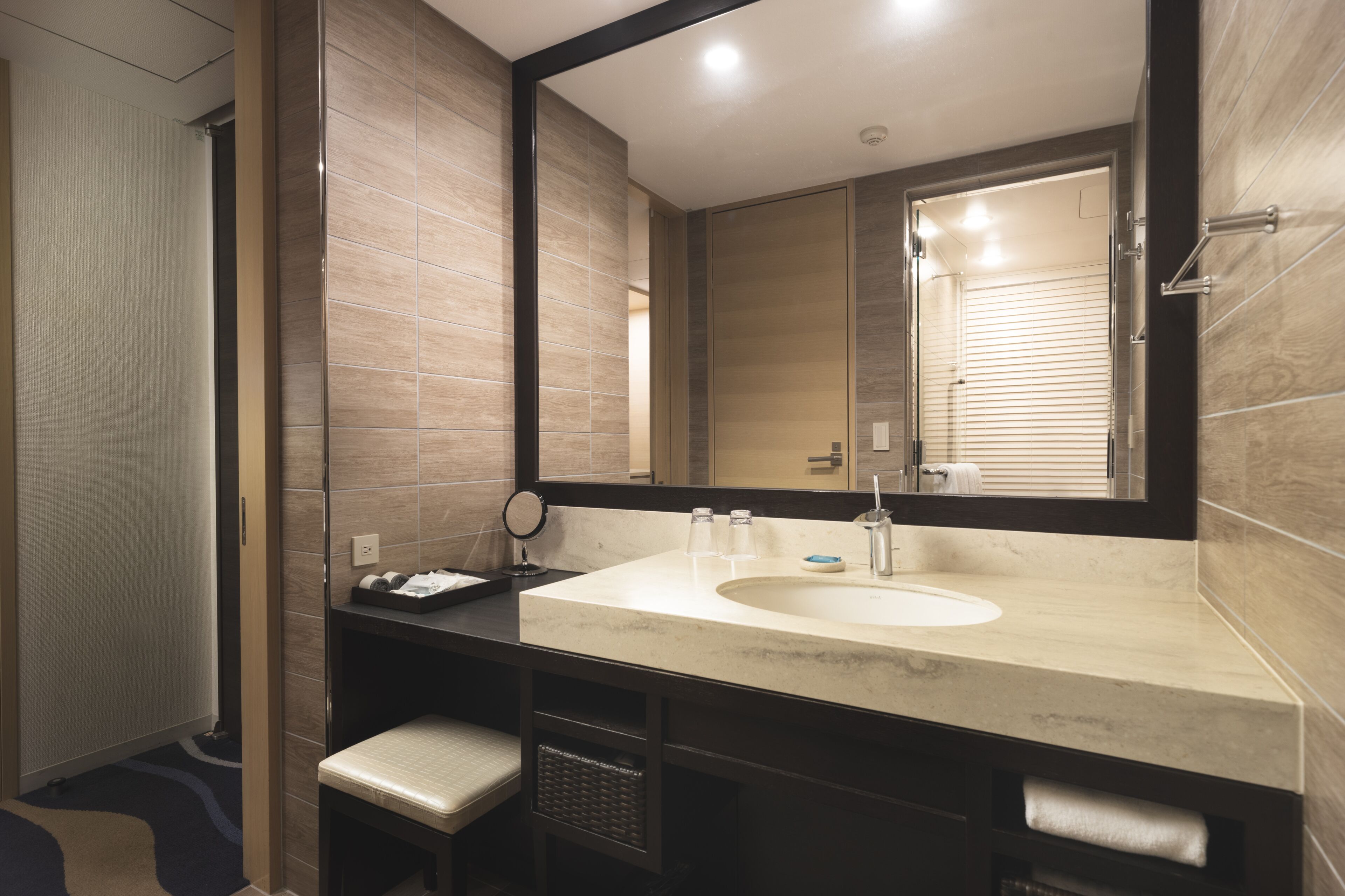 A modern bathroom with a large mirror, a sink, and a bench.