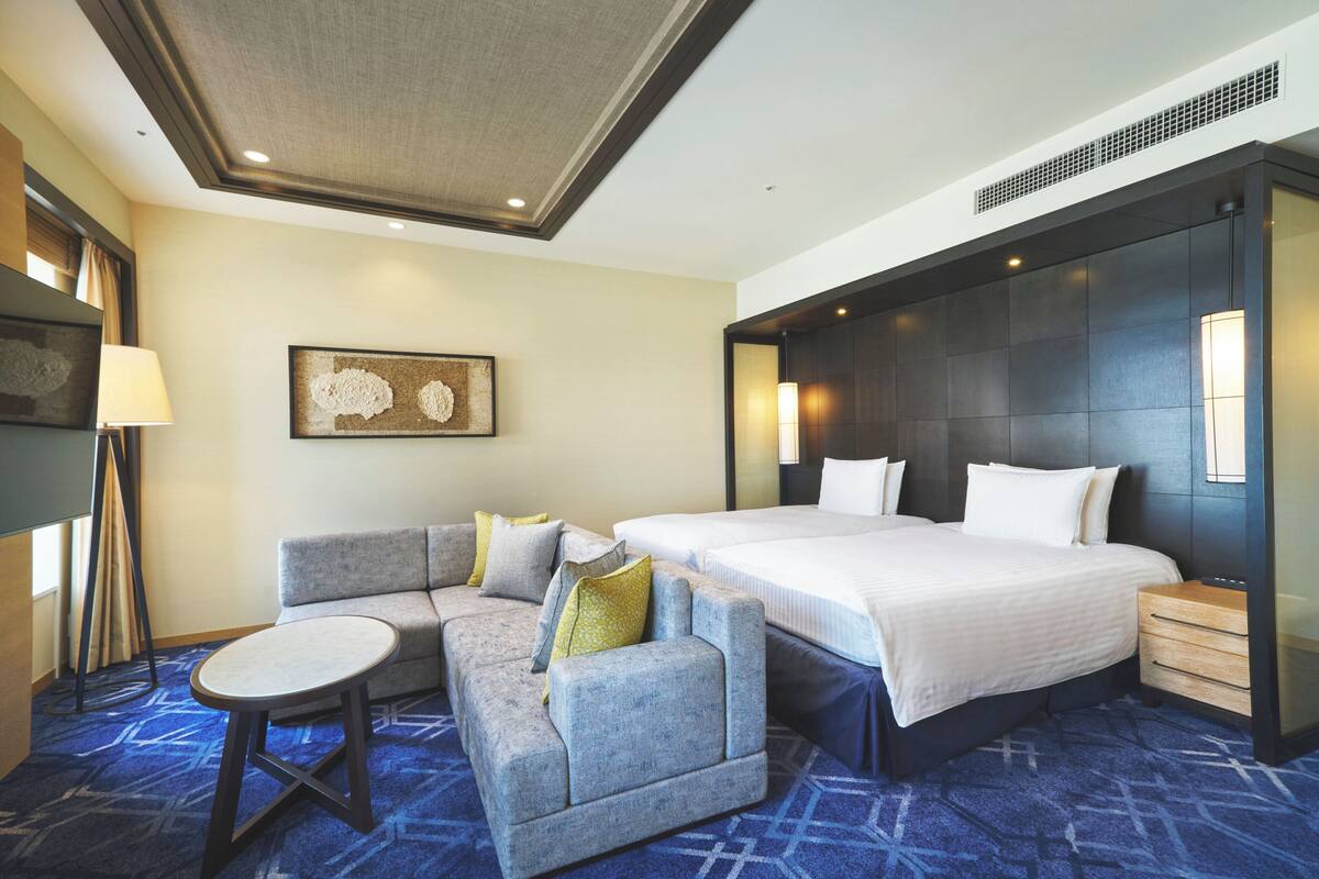 A hotel room with a large bed, a sofa, a small table, and a wall-mounted lamp.