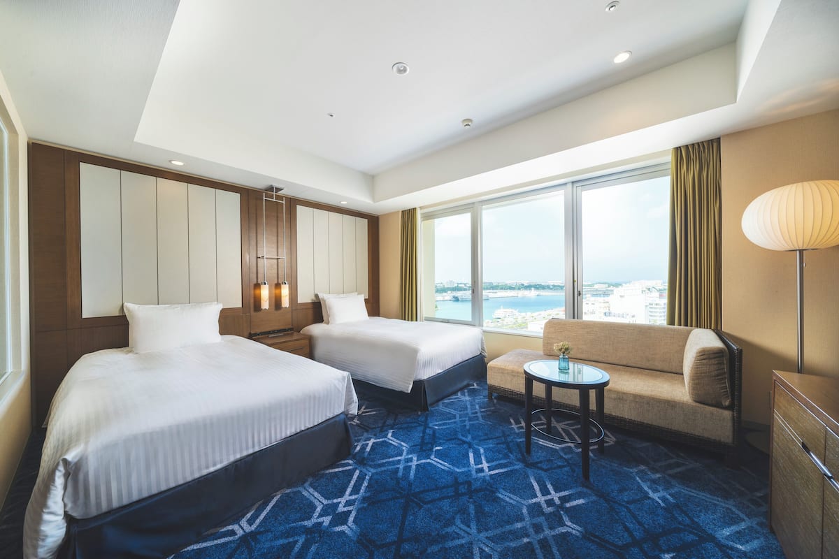 A hotel room with two beds, a sofa, a small table, and a view of the city.
