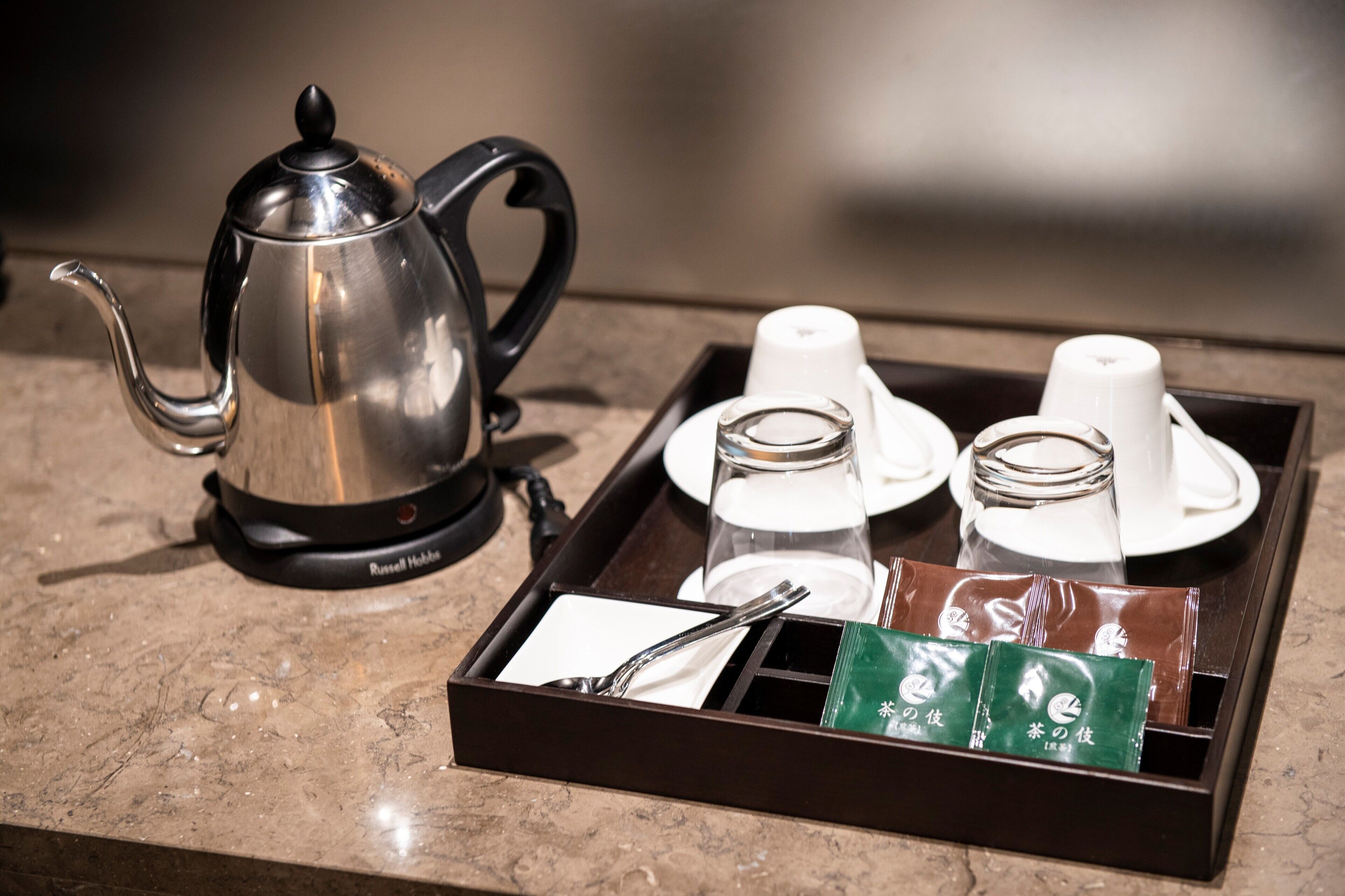 A tray with a teapot, cups, and tea packets on a marble countertop.