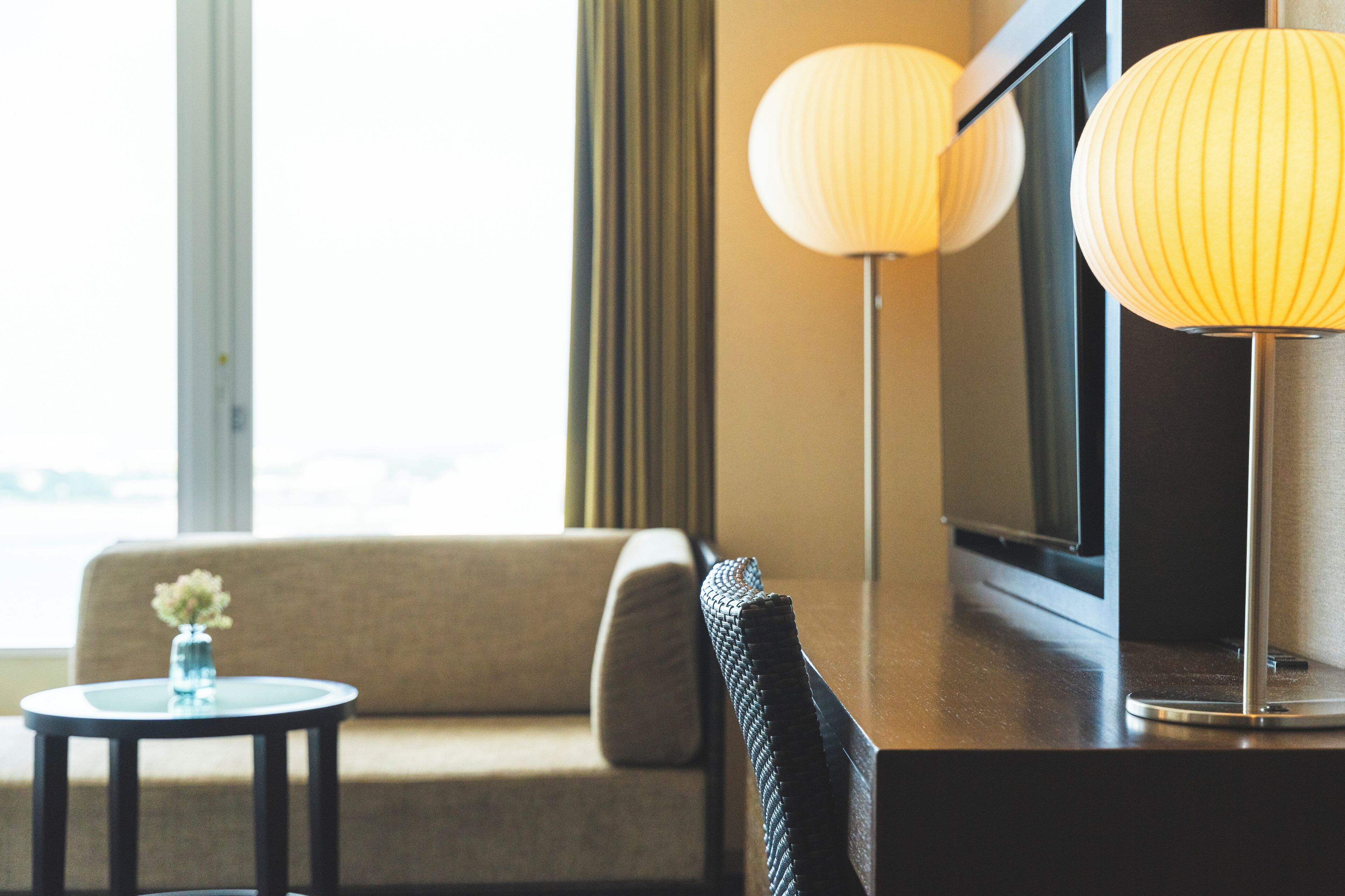 A hotel room with a sofa, a small round table with a vase, and two wall-mounted lamps.