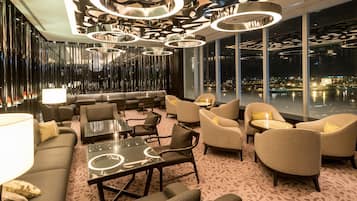 Eine moderne Lounge mit Sofas, Sesseln und Tischen, mit Blick auf die Stadt durch große Fenster.