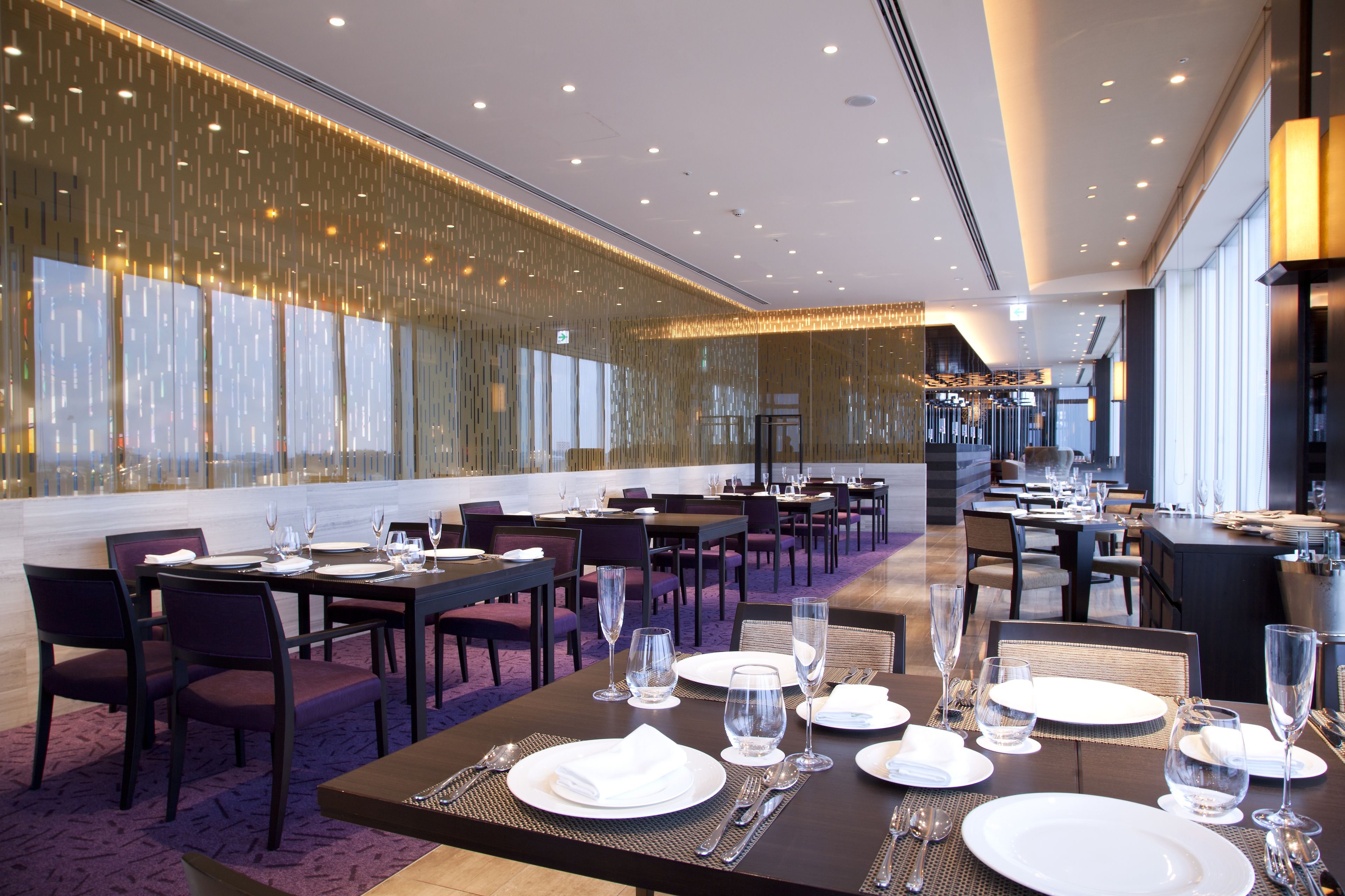 A restaurant with multiple dining tables set for service, featuring a modern interior with a patterned wall and large windows.