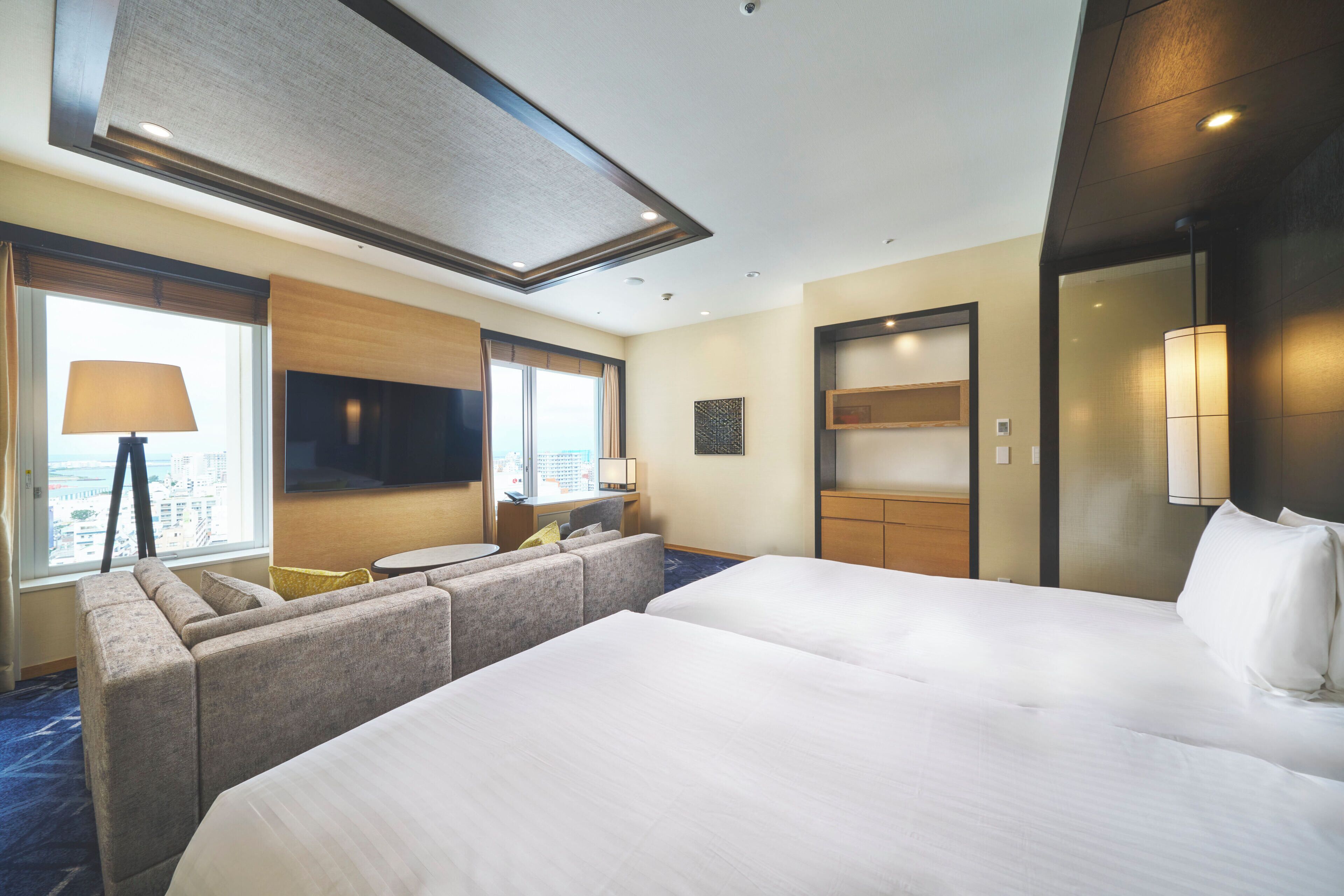 A hotel room with a large bed, a sofa, a desk, a TV, and a window with a view of the city.