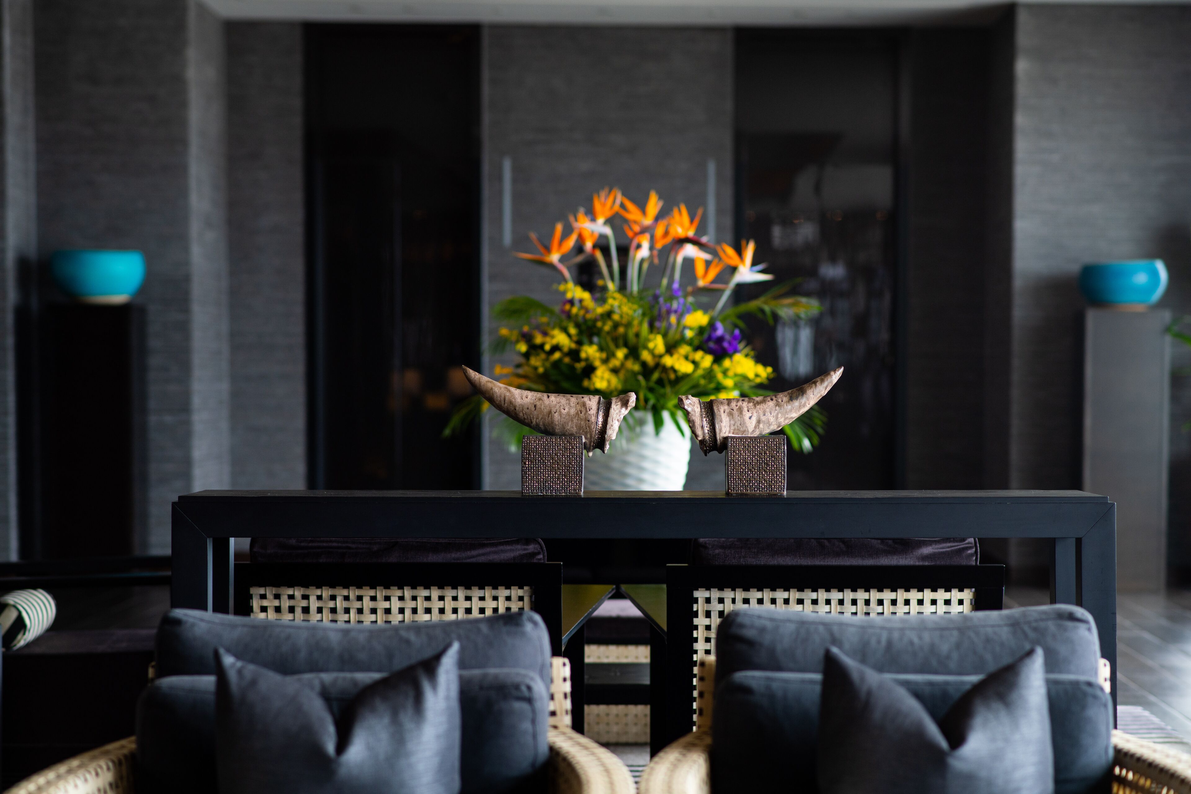 Una sala de estar moderna con un sofá oscuro, una mesa de centro con un centro de mesa floral y una decoración de estilo minimalista.