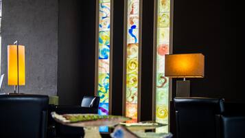 Un comedor con una mesa dispuesta para dos personas, una lámpara y un muro con paneles de vidrio emplomado de colores.