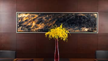 A room with a wooden panel wall, a framed abstract painting, a red vase with yellow flowers, and a black leather chair.