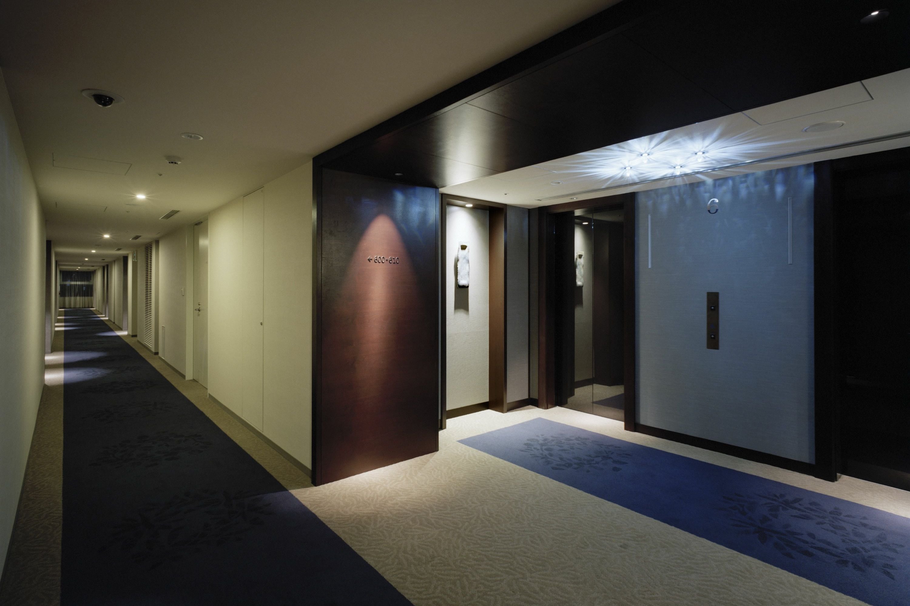 A hotel corridor with a carpeted floor, doors, and a light fixture.