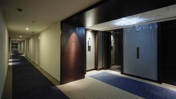 A hotel corridor with a carpeted floor, doors, and a light fixture.