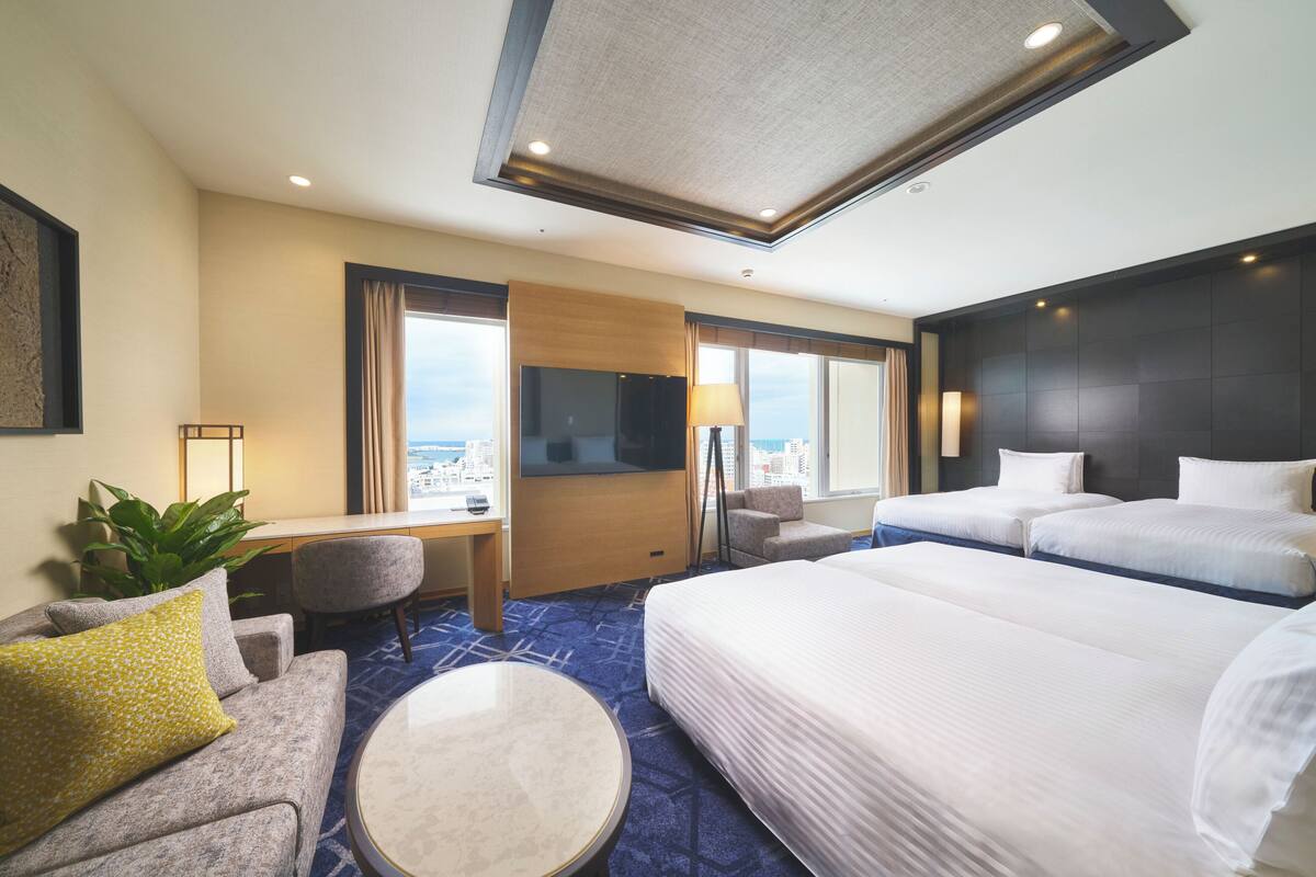 A hotel room with a large bed, a desk, a chair, a TV, and a view of the city.