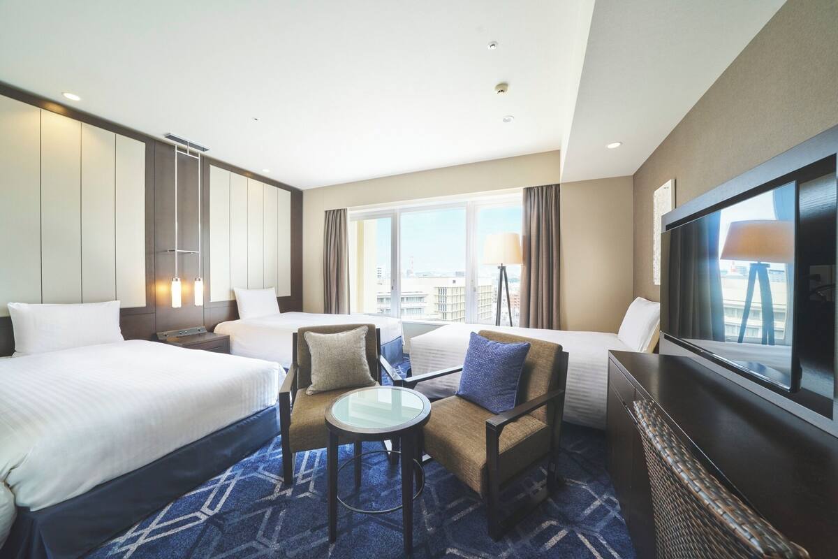A hotel room with two beds, a sofa, a small table, and a TV.