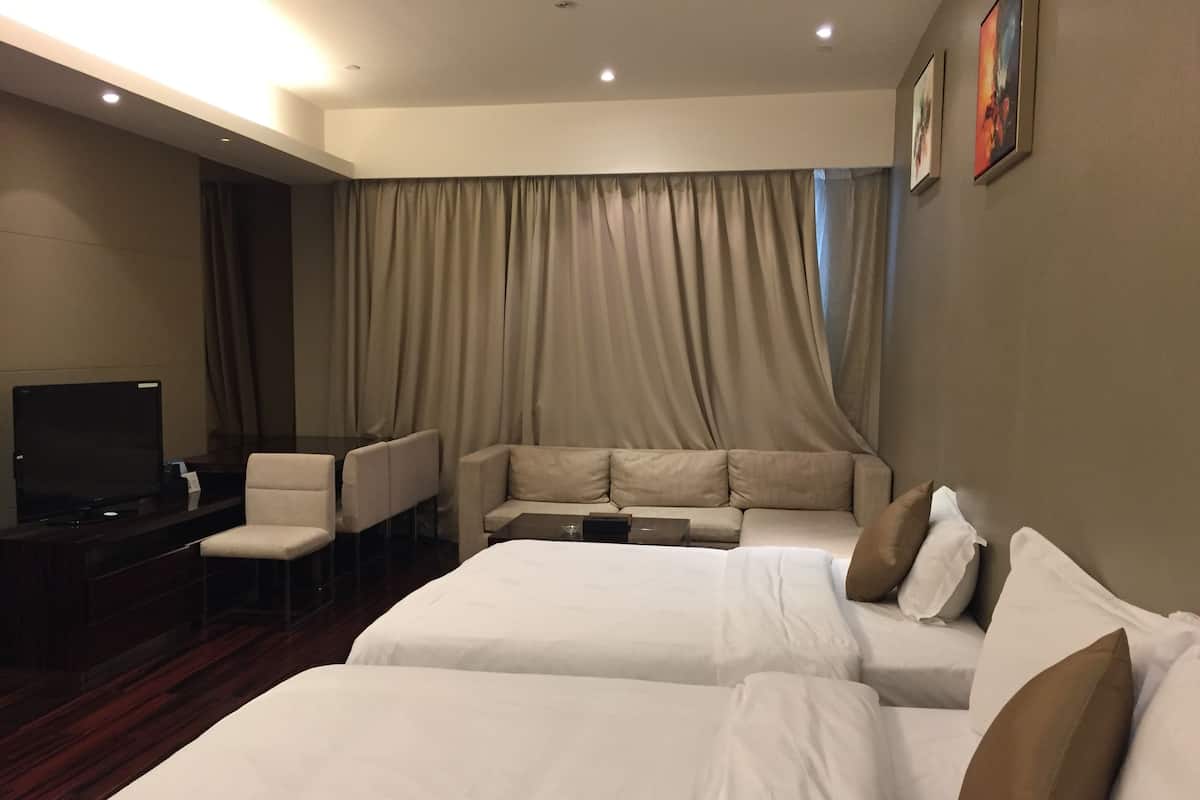 A hotel room with two beds, a sofa, a TV, and a desk.
