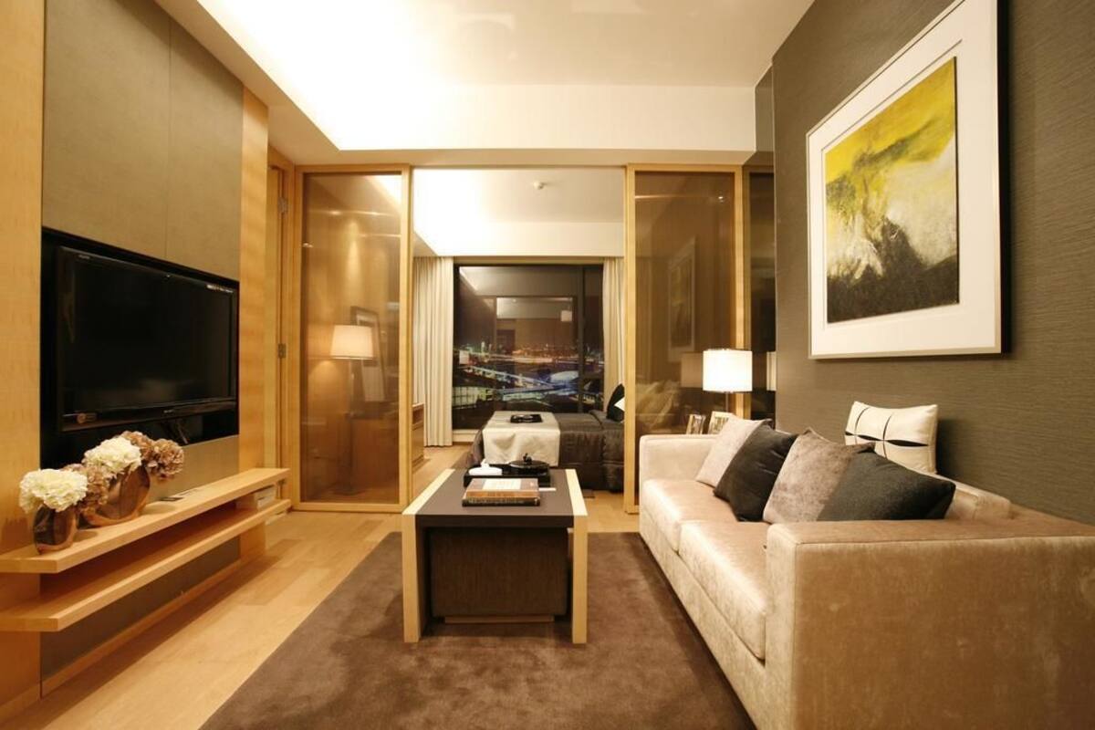 A modern hotel room with a large flat-screen TV, a sofa, a coffee table, and a painting on the wall.