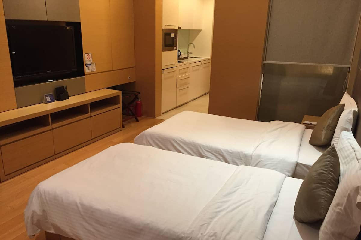 A hotel room with two beds, a TV, a small kitchenette, and a bathroom.