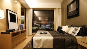 Una habitación de hotel moderna con una cama grande, un televisor de pantalla plana, un escritorio con una computadora y vistas a la ciudad desde la ventana.