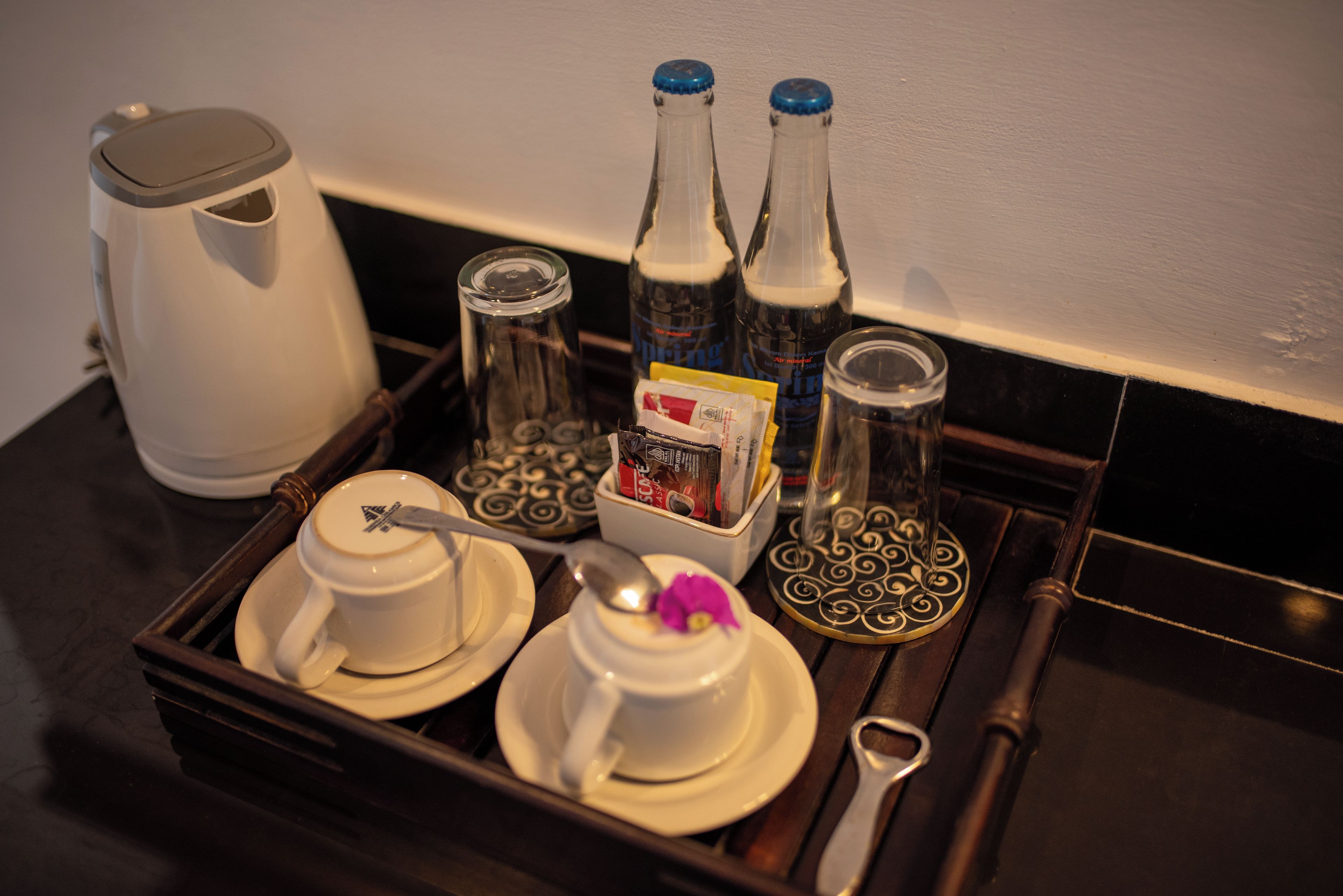 A tray with a coffee maker, two cups, a jar, and bottles on a dark surface.