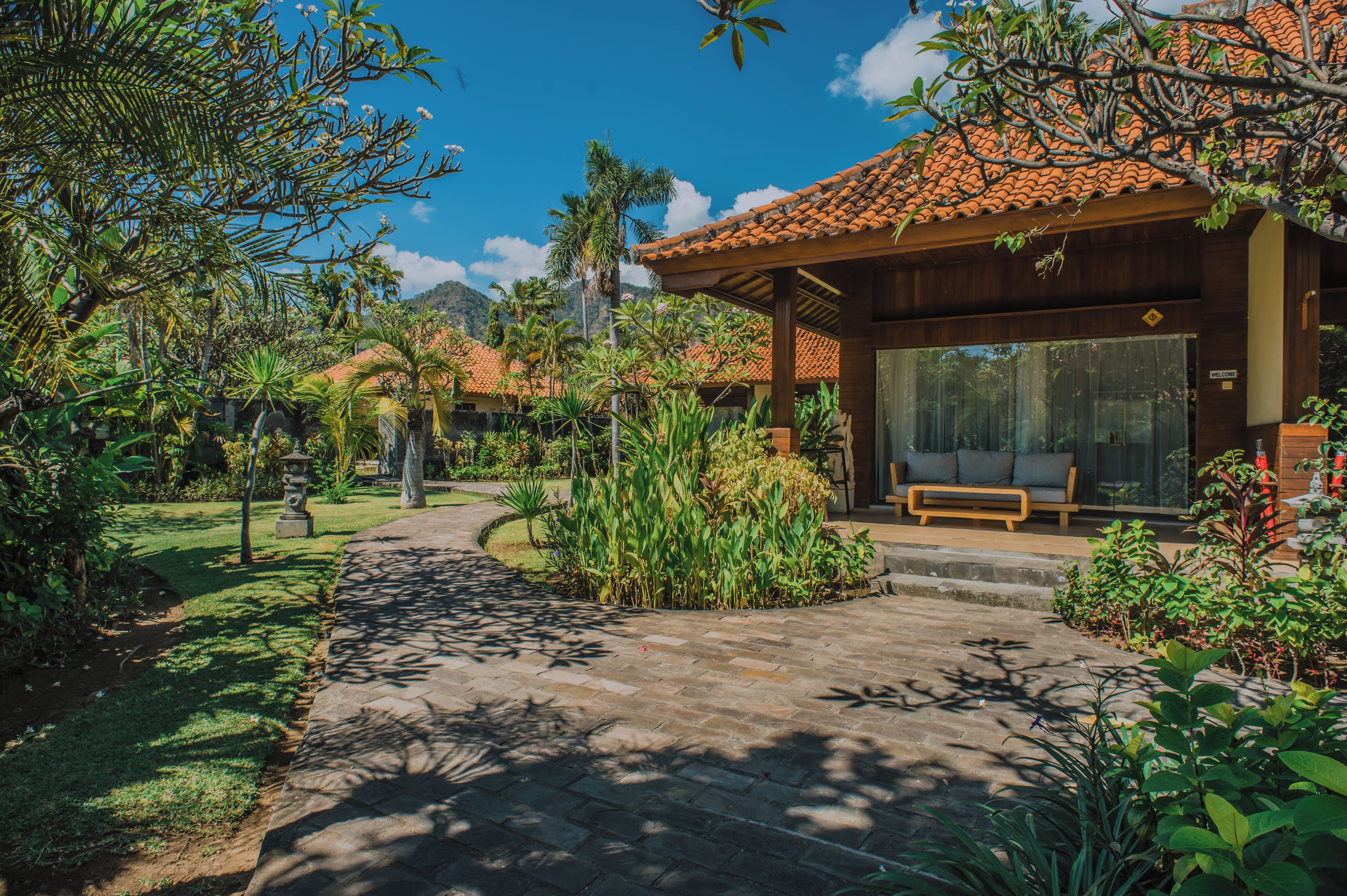 A wooden building with a tiled roof, surrounded by lush greenery and a paved pathway leading to it.