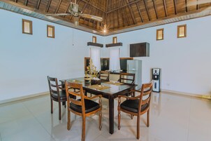 Un comedor con una mesa y sillas de madera, un ventilador de techo y un televisor en la pared.