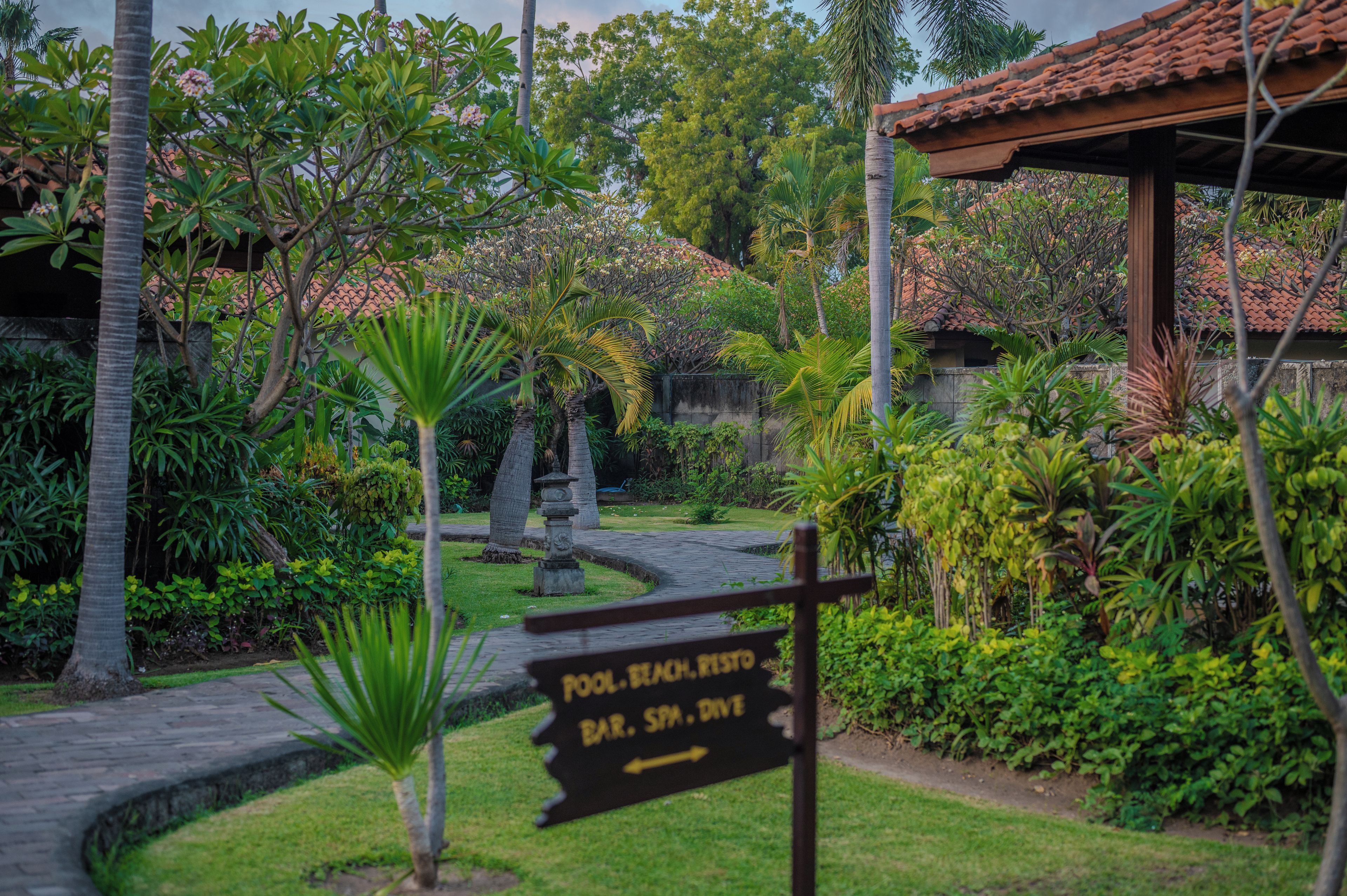 A signpost in a garden with a pathway leading to a pool, bar, spa, and drive.