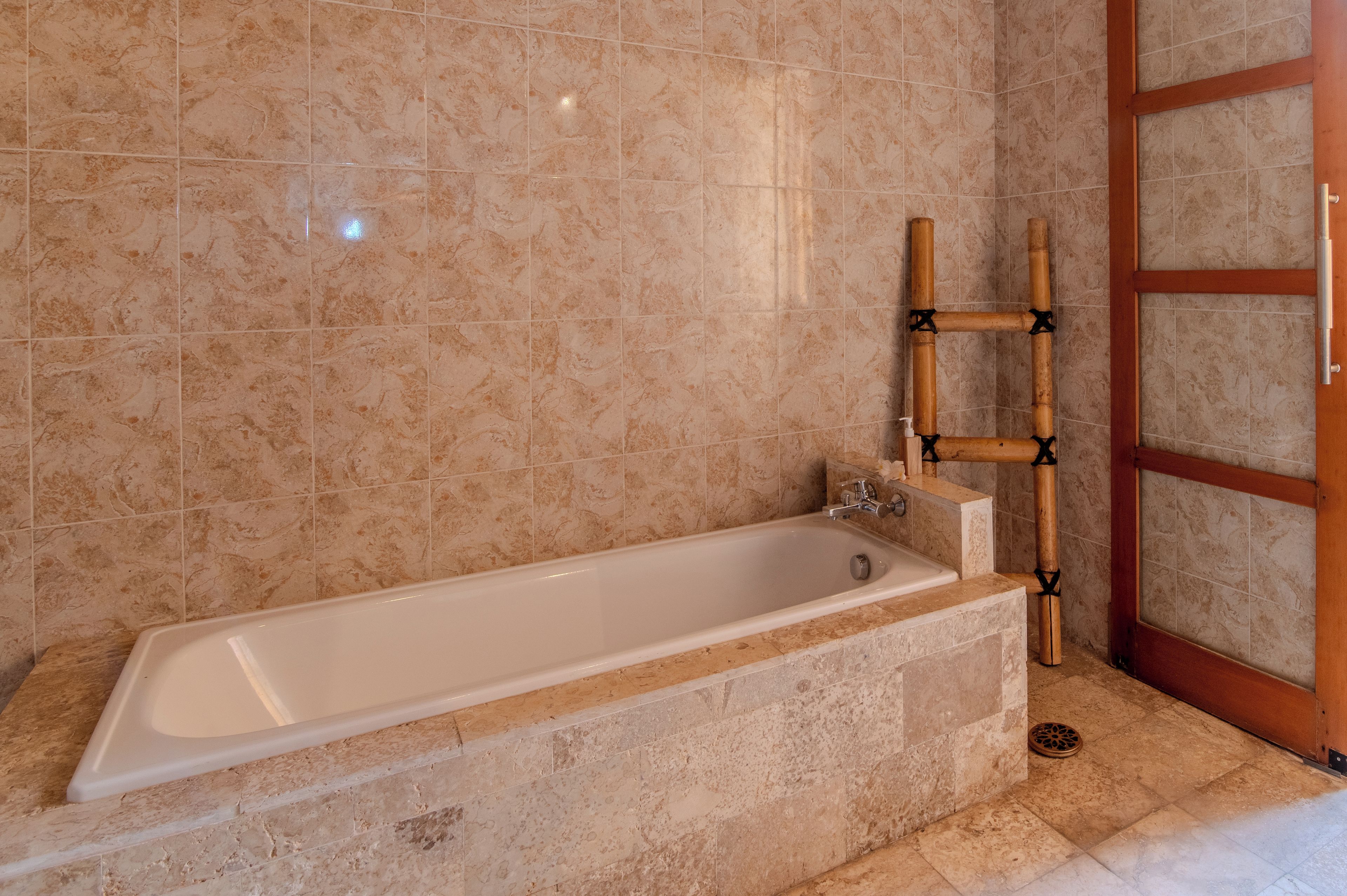 A bathroom with a bathtub, marble tiles, and a wooden door.