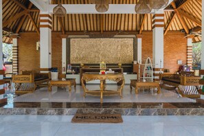 A reception area with a reception desk, seating, a decorative wall, and a welcome mat. - Adi Assri Beach Resort & Spa (Pemuteran)