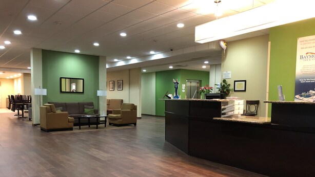 A hotel reception area with a reception desk, seating area, and a staircase leading to the elevator. - PetroStay Inn & Suites Cotulla (Cotulla)