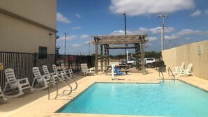 A pool area with lounge chairs, a wooden pergola, and a clear blue sky. - PetroStay Inn & Suites Cotulla (Cotulla)