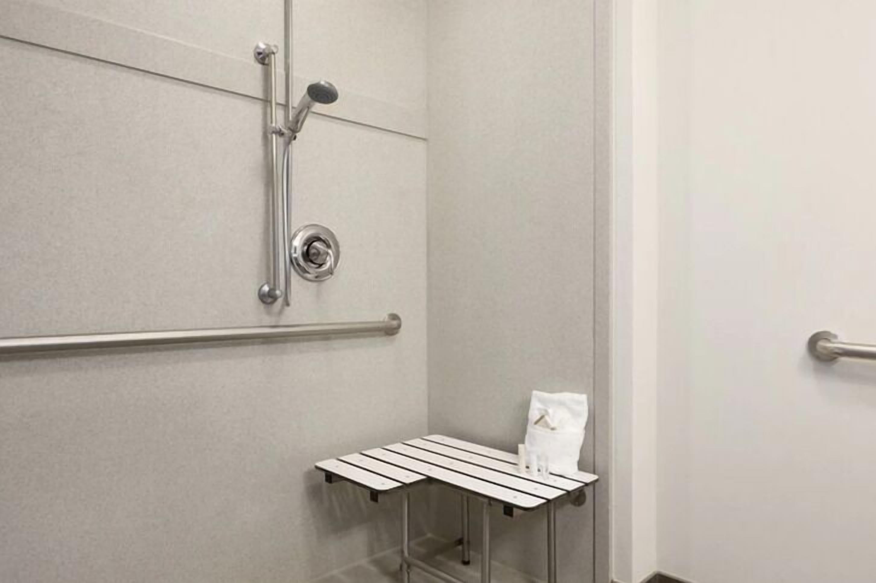 Bagno con doccia, maniglie di sostegno, porta asciugamani e un piccolo tavolo con articoli da toilette.