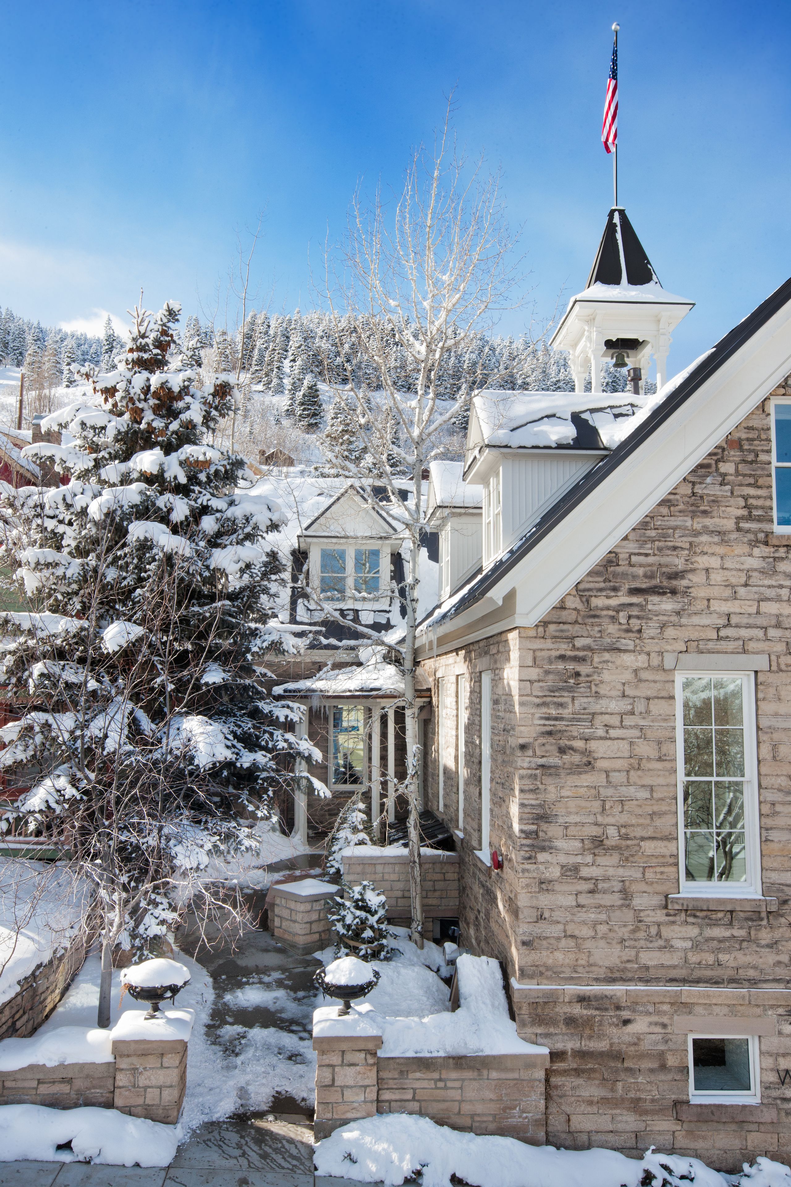A stone building with a flag, snow-covered trees, and a clear sky.