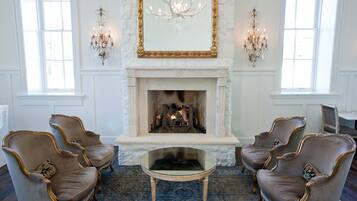 A room with a fireplace, two armchairs, a glass coffee table, and two wall sconces.