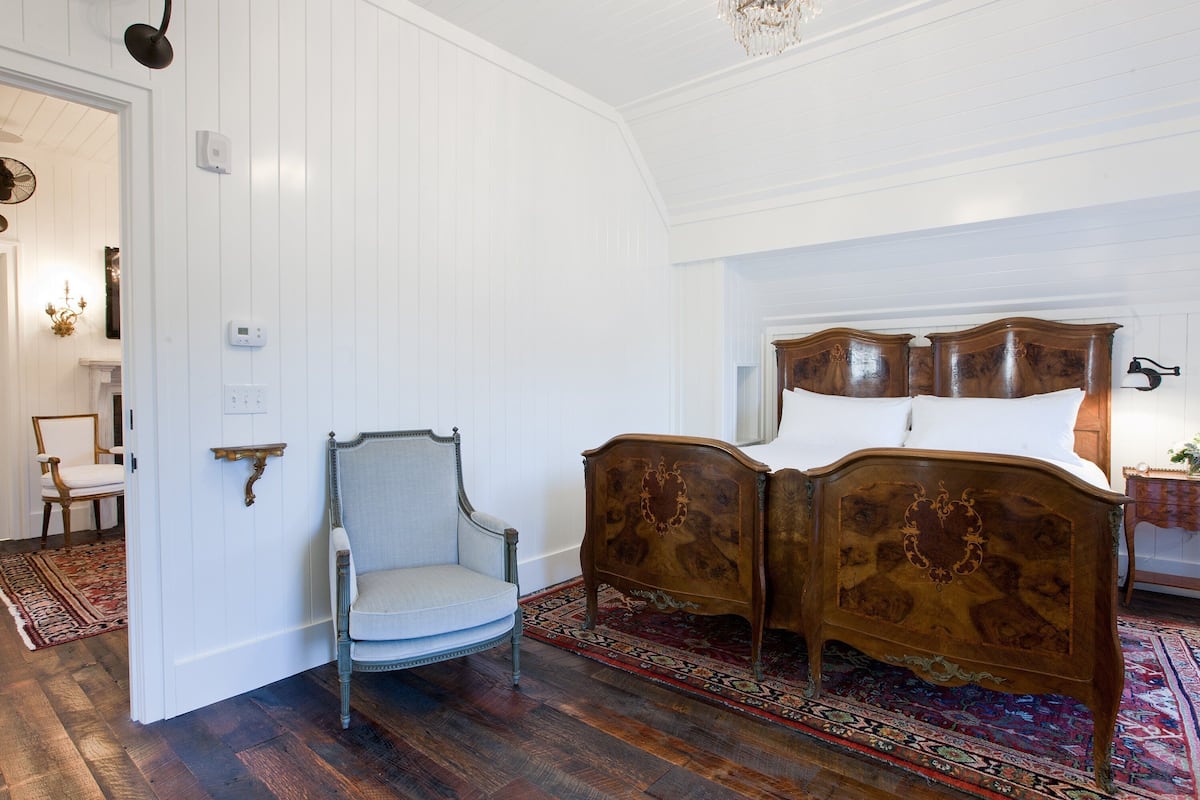 Un dormitorio con cama doble, un sillón antiguo y una alfombra estampada.