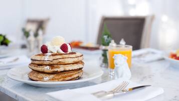 A breakfast setting with pancakes topped with whipped cream and berries, a glass of orange juice, and a salt shaker on a marble table.