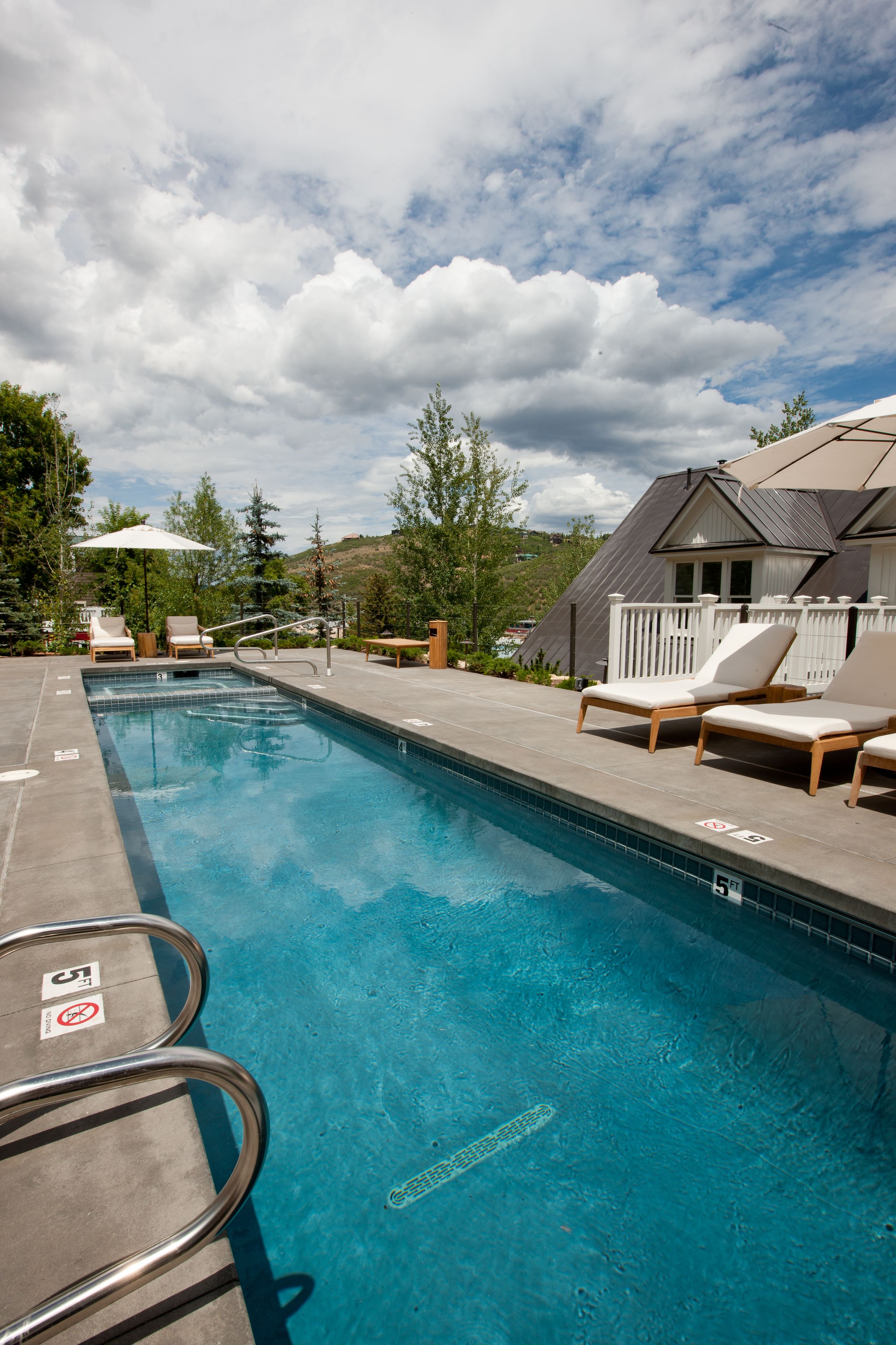 Una piscina con sillones reclinables, una terraza de madera y una cerca blanca.