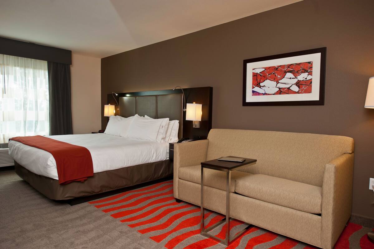 A hotel room with a bed, a sofa, a small table, and a framed picture on the wall.