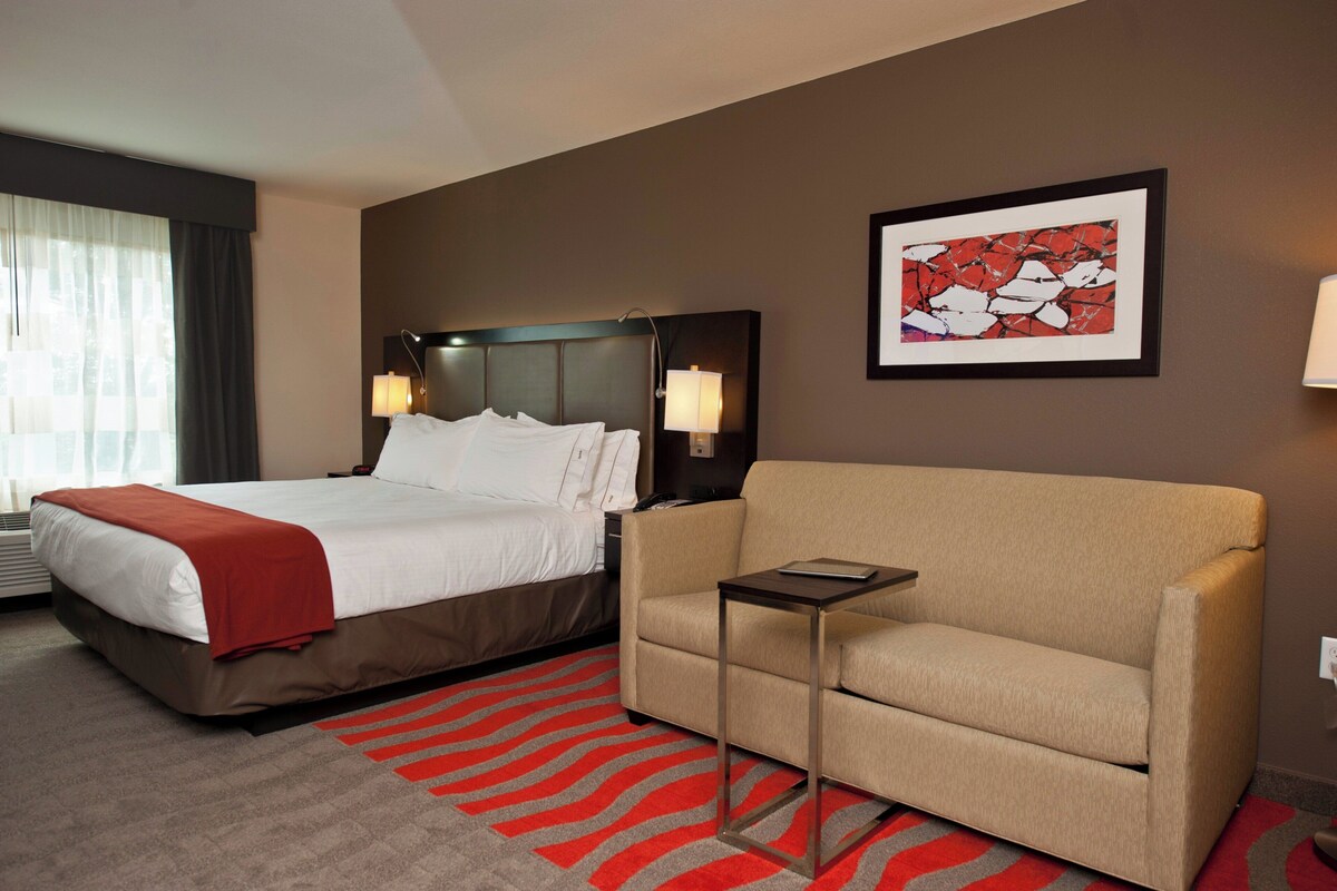 A hotel room with a bed, a sofa, a small table, and a painting on the wall.