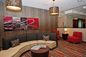 A hotel lobby with a curved sofa, a round coffee table, and a red armchair. There are abstract paintings on the wall and a reception desk in the background.