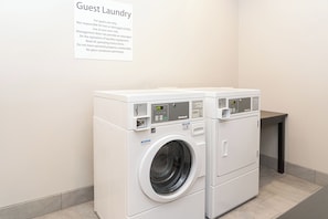 A guest laundry area with a white wall-mounted sign providing instructions and a front-loading Huebsch brand washing machine. - Holiday Inn Express & Suites Columbus - Easton Area by IHG (Columbus)