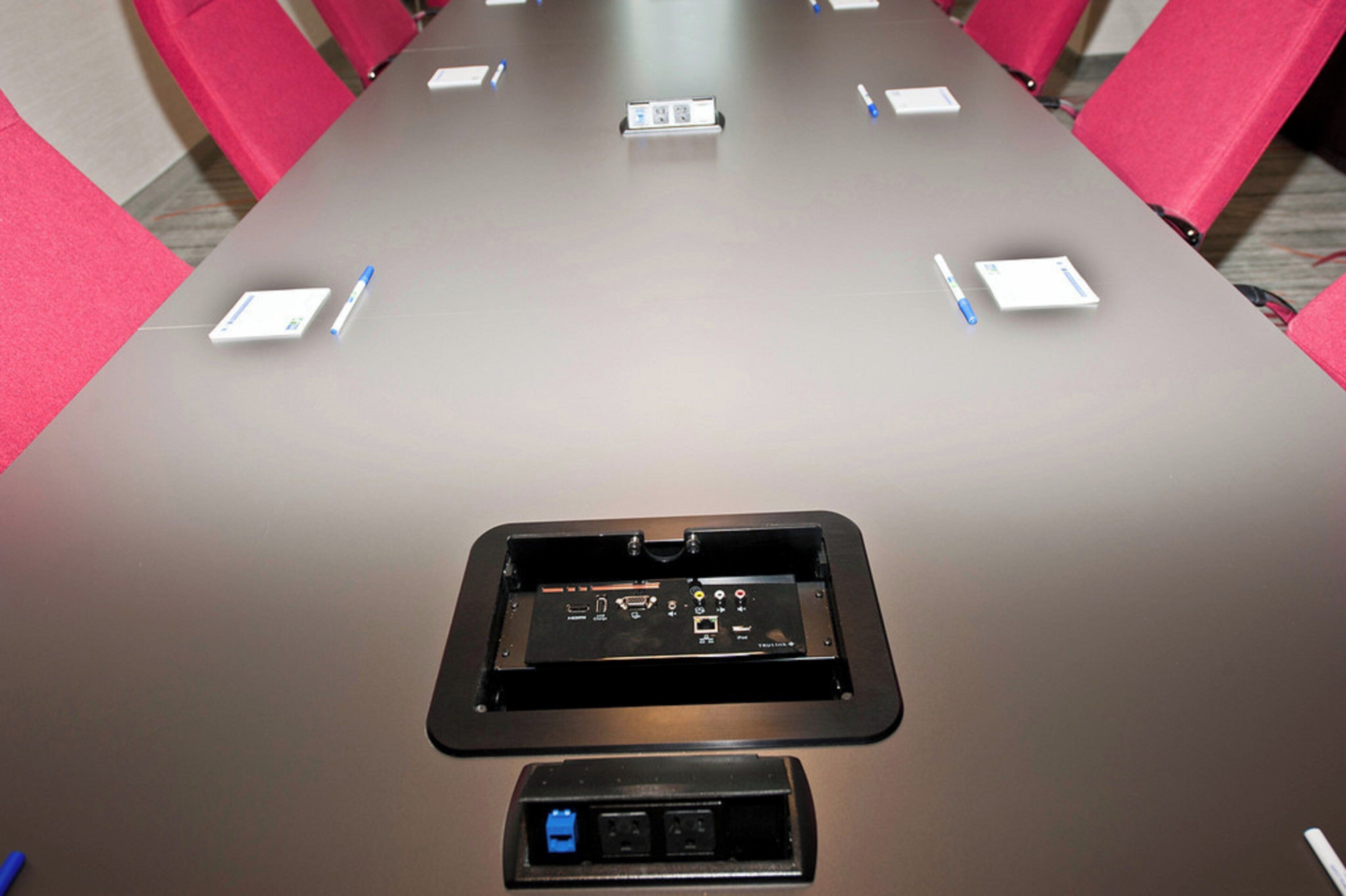 A conference table with a built-in electronic device, possibly a presentation screen, and a power outlet at the front.