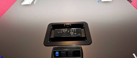 A conference table with a built-in electronic device, possibly a presentation screen, and a power outlet at the front.