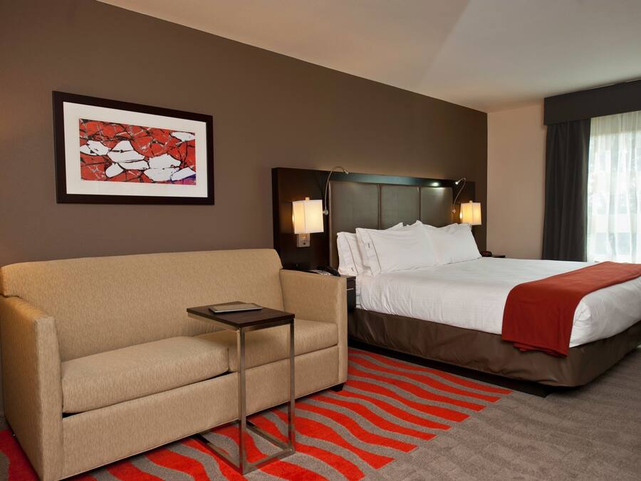 A hotel room with a bed, a sofa, a small table, a framed picture on the wall, and a window with curtains.