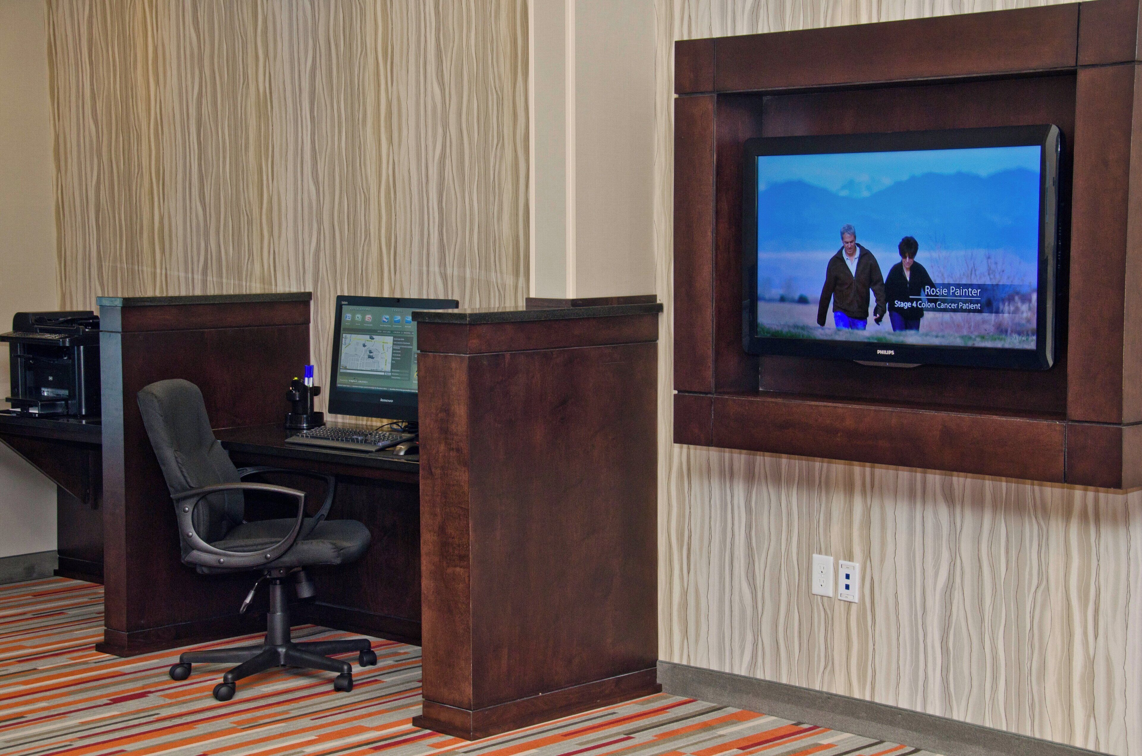A hotel room with a desk, computer, and a television mounted on the wall.